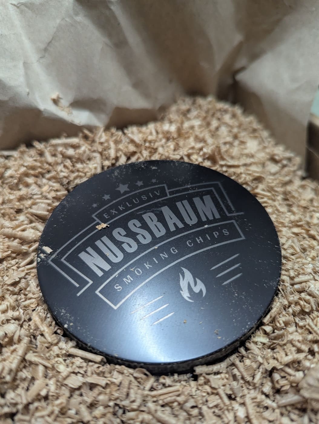Schwarze Metalldose mit Nussbaum Smoking Chips auf Holzspänen – exklusives Räucherzubehör von Wooden Axe für Grill und BBQ